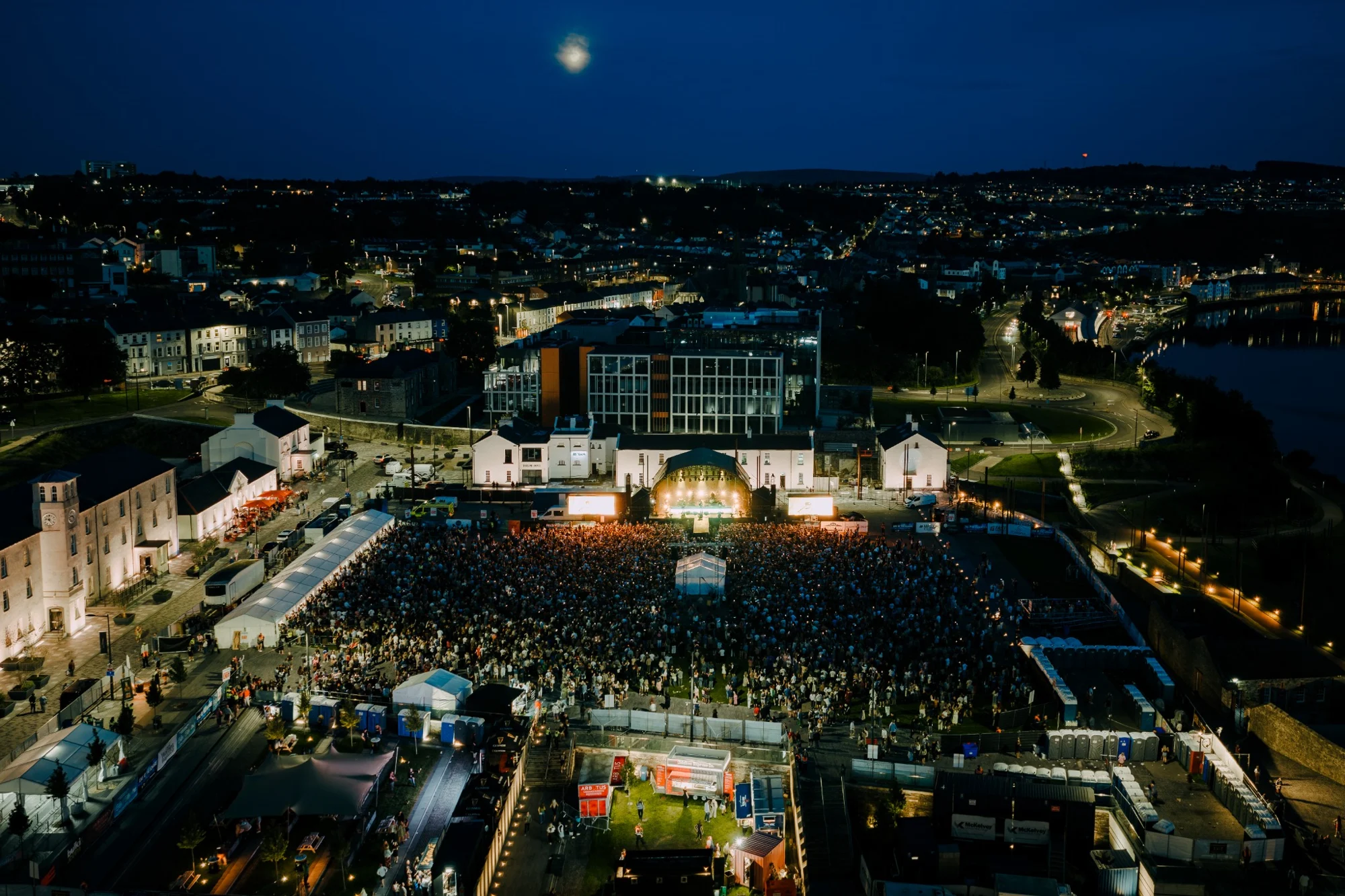 Aerial view of a packed Ebrington Square at night, with Derry beyond